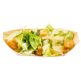 A biodegradable pinewood boat serves as the tray, holding a Caesar salad with romaine lettuce, croutons, shredded parmesan cheese, and parsley sprigs, all arranged neatly on a white background.