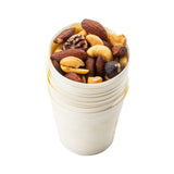 A small stack of eco-friendly, light-colored disposable serving cups filled with a mix of almonds, cashews, walnuts, and hazelnuts sits on a white background. The biodegradable cups are neatly nested, showcasing the nuts on top.