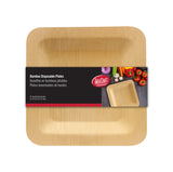 A square, disposable bamboo plate with a natural finish is packaged with a black label. The label displays the TableCraft logo, product name in three languages, and an image of vegetables beside the plate. Rounded corners and wood grain texture complete the look.