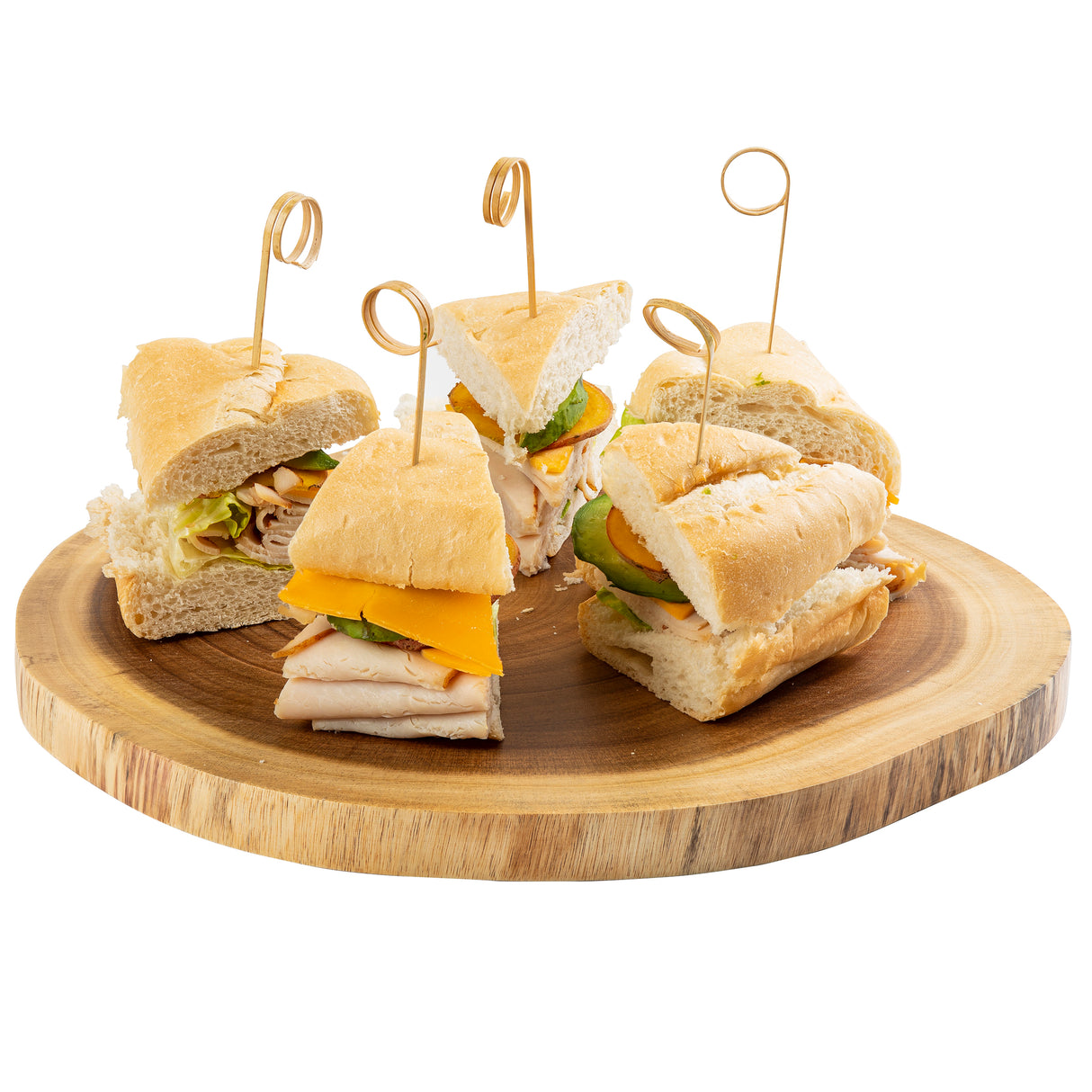 Five sandwich quarters made with baguette, turkey, cheddar cheese, and lettuce are arranged on a round wooden serving board. Each is secured with a decorative TableCraft bamboo card holder pick. The background is plain white.