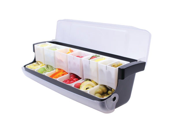 A black and gray garnish station with a clear lid, featuring six transparent compartments for sliced lemons, limes, orange slices, cherry tomatoes, olives, and assorted garnishes; NSF certified and ideal for first in first out use.