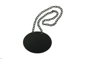 A black, round, flat Chalkboard Necklace pendant hangs from a matching black chain. The pendant has two holes at the top for the chain to loop through. The plain white background highlights its simple, modern TableCraft Products-inspired design.