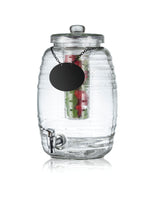 A clear ribbed glass beverage dispenser with a spigot at the bottom, lid on top, and black round label on a chain. Inside, cucumber, strawberries, and mint infuse the water. The background is white—perfect as a stylish TableCraft Beehive Beverage Dispenser.