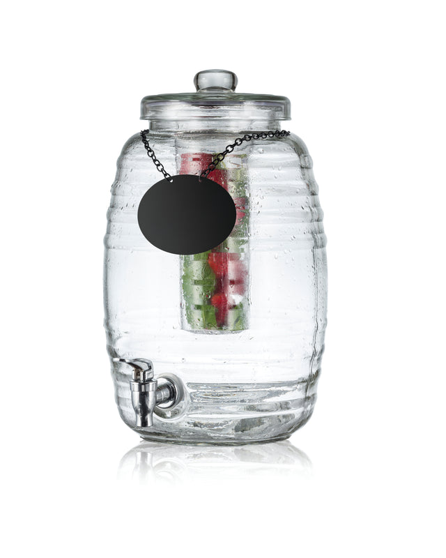 A clear ribbed glass beverage dispenser with a spigot at the bottom, lid on top, and black round label on a chain. Inside, cucumber, strawberries, and mint infuse the water. The background is white—perfect as a stylish TableCraft Beehive Beverage Dispenser.