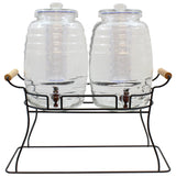 Two clear glass beverage dispensers with round lids and spigots sit side by side on a black powder coated metal base with wooden handles. The double beverage dispenser features a ribbed design and internal cylindrical infusers for easy and stylish serving.
