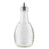 This clear glass bottle from the Beehive Collection features horizontal ridges and a cone-shaped metal pour spout. Perfect as an Oil/Vinegar Dispenser, it stands empty and upright on a white background, ideal for any TableCraft Products display.