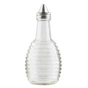 This clear glass bottle from the Beehive Collection features horizontal ridges and a cone-shaped metal pour spout. Perfect as an Oil/Vinegar Dispenser, it stands empty and upright on a white background, ideal for any TableCraft Products display.