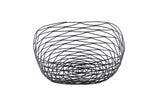 A modern, black powder coated metal basket from the Artisan Collection Basket line. Its open, geometric wire design forms a spiral pattern in a rounded, bowl-like shape. The empty TableCraft BK17310 is displayed on a plain white background.
