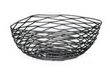 A black powder coated metal basket with an open, geometric design featuring wavy, crisscrossing lines. This Artisan Collection Basket by TableCraft BK17310 has an irregular shape and casts unique patterned shadows on the white surface below.