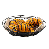 A black powder coated metal Artisan Collection Basket holds three golden, glossy croissants drizzled with chocolate, resting on a folded beige napkin. The croissants look fresh and appetizing, with rich chocolate lines accentuating their flaky texture.