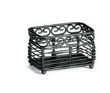A rectangular, black metal basket from the Mediterranean Collection by TableCraft, featuring decorative swirl patterns. This sturdy Sugar Packet Holder has an open, slatted design with small round feet and is photographed on a white background.