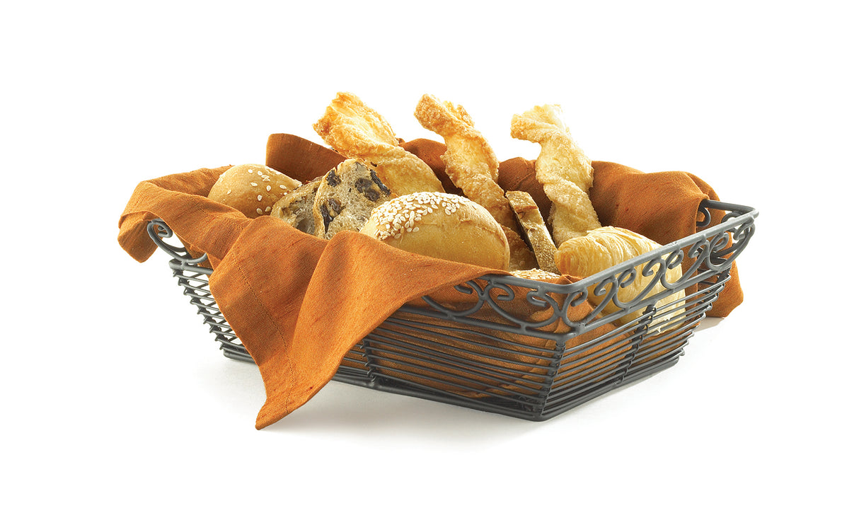 A powder coated metal basket lined with orange cloth holds assorted breads, including sesame-coated rolls, breadsticks, and pastries, all arranged neatly against a white background.