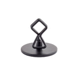 A black, powder coated metal Number/Card Holder Stand with a round flat base and an abstract geometric figure on top. The figure features a triangular lower section and diamond-shaped upper section, both crafted from bent metal rods.
