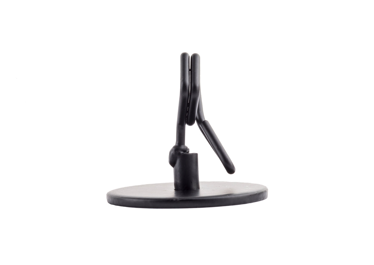 A small, black, powder coated metal Number/Card Holder Stand with a circular base and upright clip mechanism, photographed against a plain white background. The simple, functional design is ideal for holding cards, photos, or notes upright.