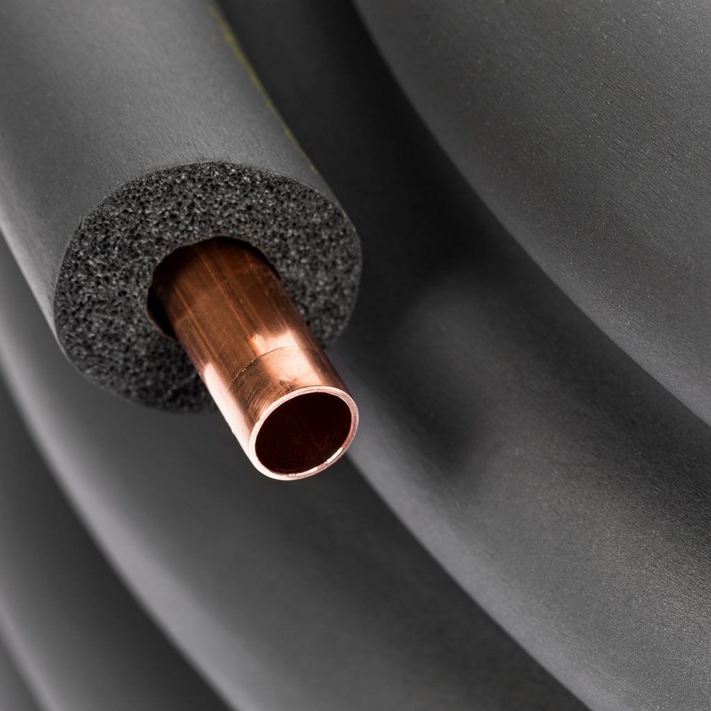 Close-up of a copper pipe partially inserted into thick, black RC54 tubing insulation. The background shows coiled foam, suggesting use in plumbing or HVAC—ideal for pairing with a CVDF-3000 condensing unit in a 50 ft. length to prevent heat loss or condensation.