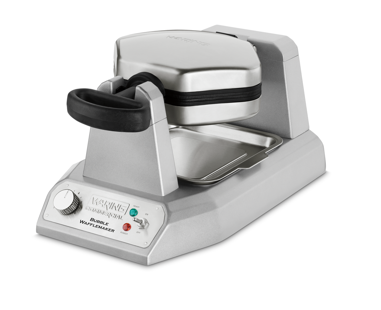 A silver, stainless steel Waring WBW300XCE Double Belgian Waffle Maker with a black handle and base. It features indicator lights, a rotary knob on the front, a deep drip tray below, and is designed for international use. The waffle plates are clamped shut.