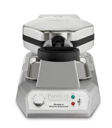 A silver Waring WBW300XCE Bubble Waffle Maker with a black handle is shown from the front. The control panel features a timer knob, indicator lights, and labeled buttons for ready, heating, and power. Ideal for international use with a sturdy design.