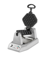 A silver bubble waffle maker with a hexagonal, open clamshell design. The black, non-stick plates have a bubble pattern. The control panel of this commercial waffle maker features a knob, indicator lights, and text. A removable tray sits underneath.
