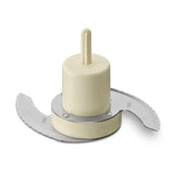 A close-up of a Waring WCG75 Chopping Blade shows two curved, sharp metal blades attached to a cream-colored plastic center hub and shaft, set against a white background. The hub has embossed text and the blades feature fine serrated edges.