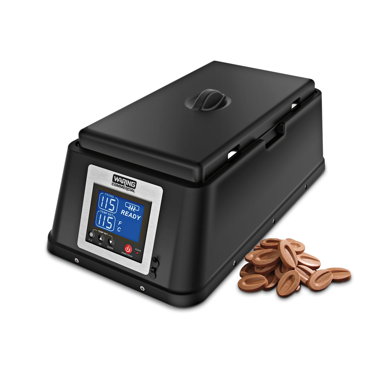 A black rectangular chocolate melter with a digital display showing temperature settings sits on a white countertop. Next to it, a small pile of oval-shaped milk chocolate pieces is arranged neatly.
