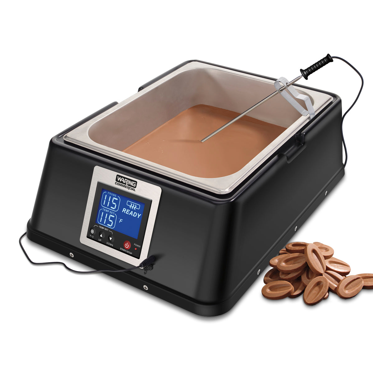 A black electric chocolate melter with a stainless steel bowl and digital display (115°F, READY) sits on the countertop, filled with melted chocolate. A temperature probe is inserted; oval milk chocolate pieces are scattered beside the machine.