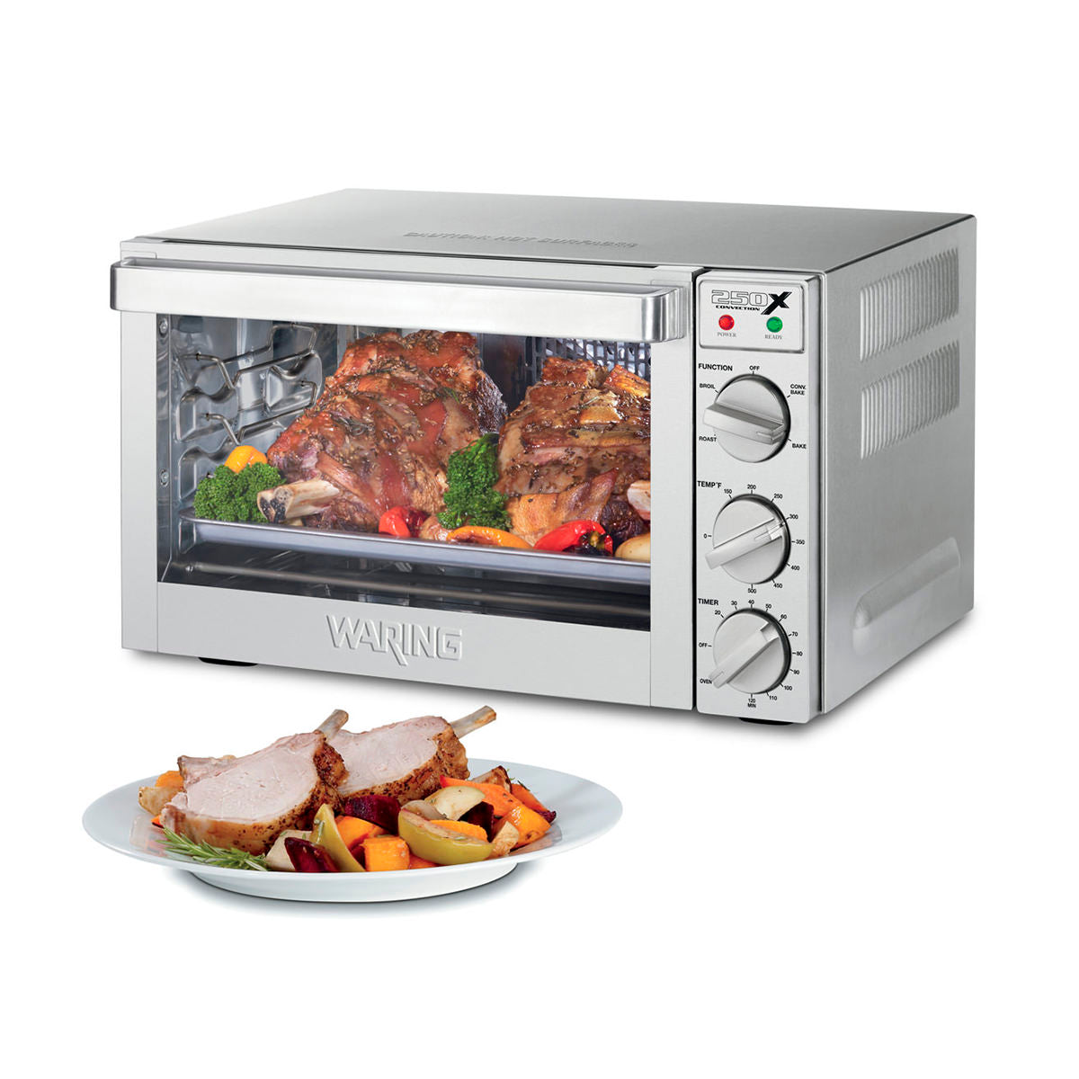 A stainless steel commercial convection oven with roast meat and vegetables inside, viewed through a glass door. Three control knobs and indicator lights are on the right. In front, a plate holds two slices of roasted meat and assorted vegetables.