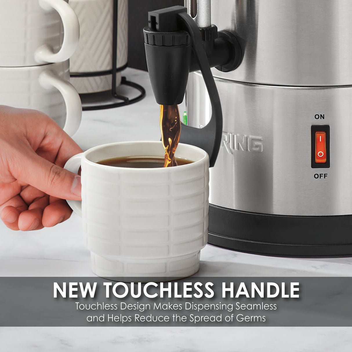 A hand holds a white textured mug under a black touchless dispenser on a stainless steel Coffee Urn with dual heater system. Coffee pours into the mug. Stacked mugs sit nearby on a marble countertop. Text: NEW TOUCHLESS HANDLE...helps reduce the spread of germs.
