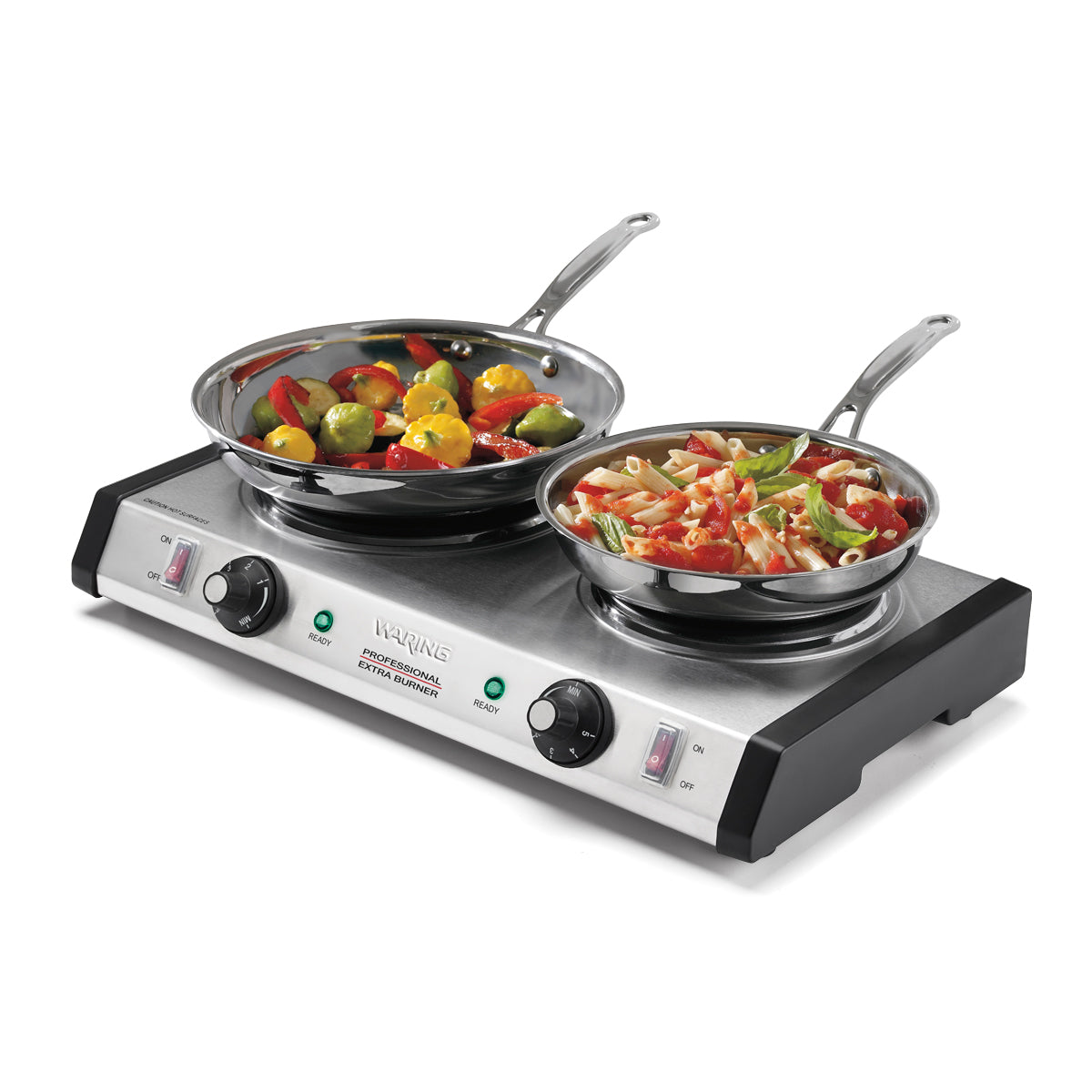 A double-burner electric hot plate with heavy-duty cast iron burners sits on a white surface. One pan holds cooked vegetables, the other pasta with vegetables. The IRVING hot plate features control knobs and indicator lights on the front.