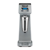 The Waring WDM120TX Single Spindle Drink Mixer features a digital display, control buttons, and a stainless steel mixing cup at the center. This sturdy countertop appliance boasts a modern, professional appearance for any kitchen or bar.
