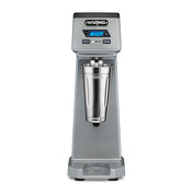 The Waring WDM120TX Single Spindle Drink Mixer features a digital display, control buttons, and a stainless steel mixing cup at the center. This sturdy countertop appliance boasts a modern, professional appearance for any kitchen or bar.