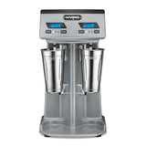 A countertop Waring drink mixer with a double spindle design features two stainless steel mixing cups, digital timers, and control buttons on a metallic base. Each side offers separate displays showing 0:40 and buttons for speed, pulse, and power.
