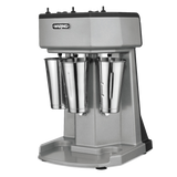 A silver Waring triple spindle Drink Mixer with three metal blending cups, black controls on top, and a sturdy base, set against a plain white background.