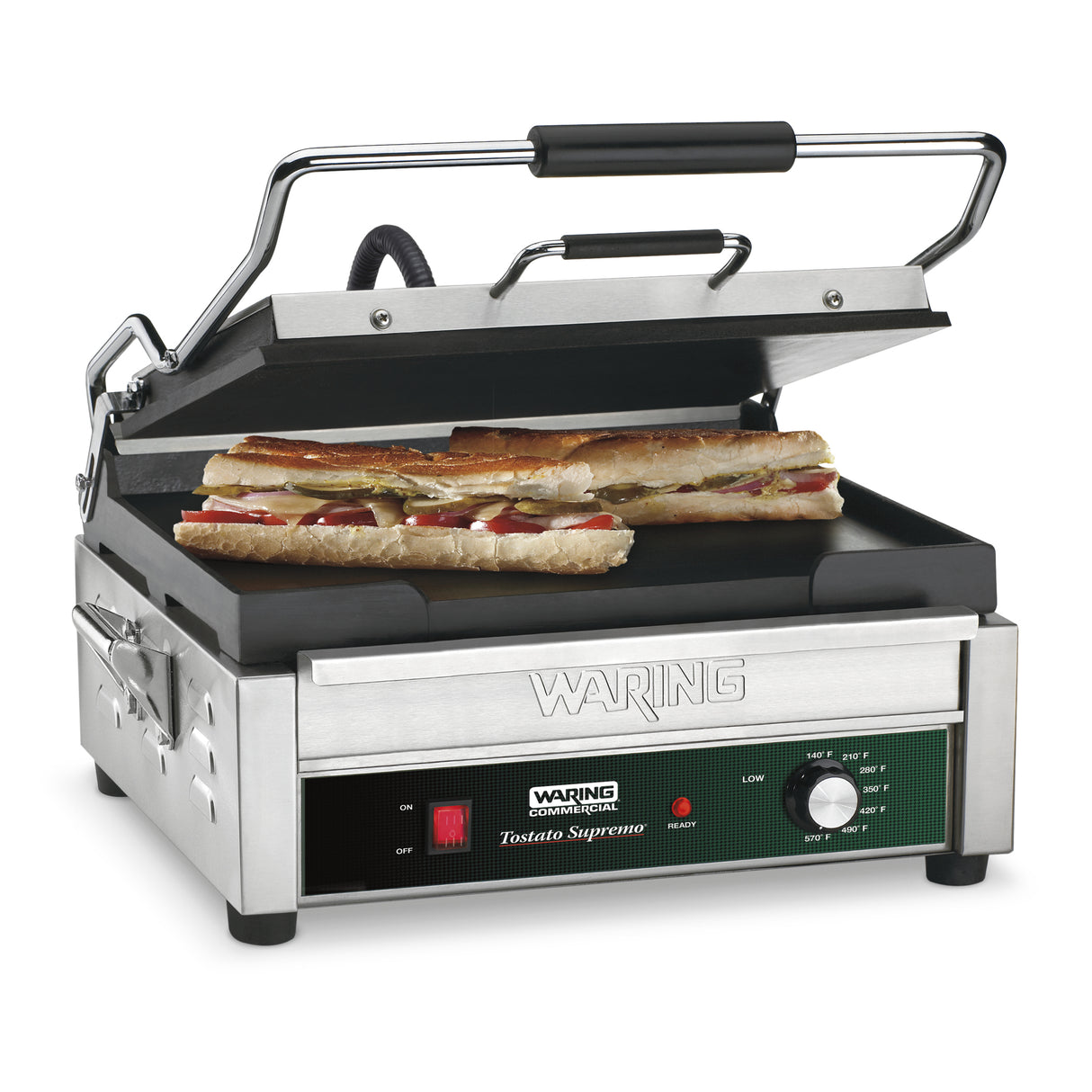 A stainless steel Waring Panini Grill with a cast iron cooking surface and partially open lid grills two long sandwiches. The control panel displays an adjustable thermostat and the label Waring Commercial Tostato Supremo. Fillings like meat and cheese are visible.