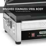 A close-up of a Waring Commercial Tostato Supremo Panini Grill with a brushed stainless steel body, cast iron cooking surface, removable drip tray, and red power switch. Text overlay reads, Brushed Stainless Steel Body with Removable Drip Tray.