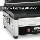 Close-up of a brushed stainless steel Panini Grill with a removable drip tray. The image highlights its sturdy metal construction, black power switch, label, and cast iron cooking surface. Overlay text reads, Brushed Stainless Steel Body.