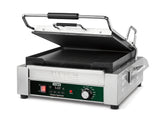 A stainless steel Panini Grill with a black handle, open to reveal flat cast iron plates. The front panel displays a programmable timer, temperature dial, and indicator lights. The brand Waring is visible above the control panel.