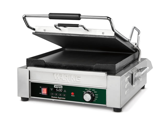 A stainless steel Panini Grill with a black handle, open to reveal flat cast iron plates. The front panel displays a programmable timer, temperature dial, and indicator lights. The brand Waring is visible above the control panel.