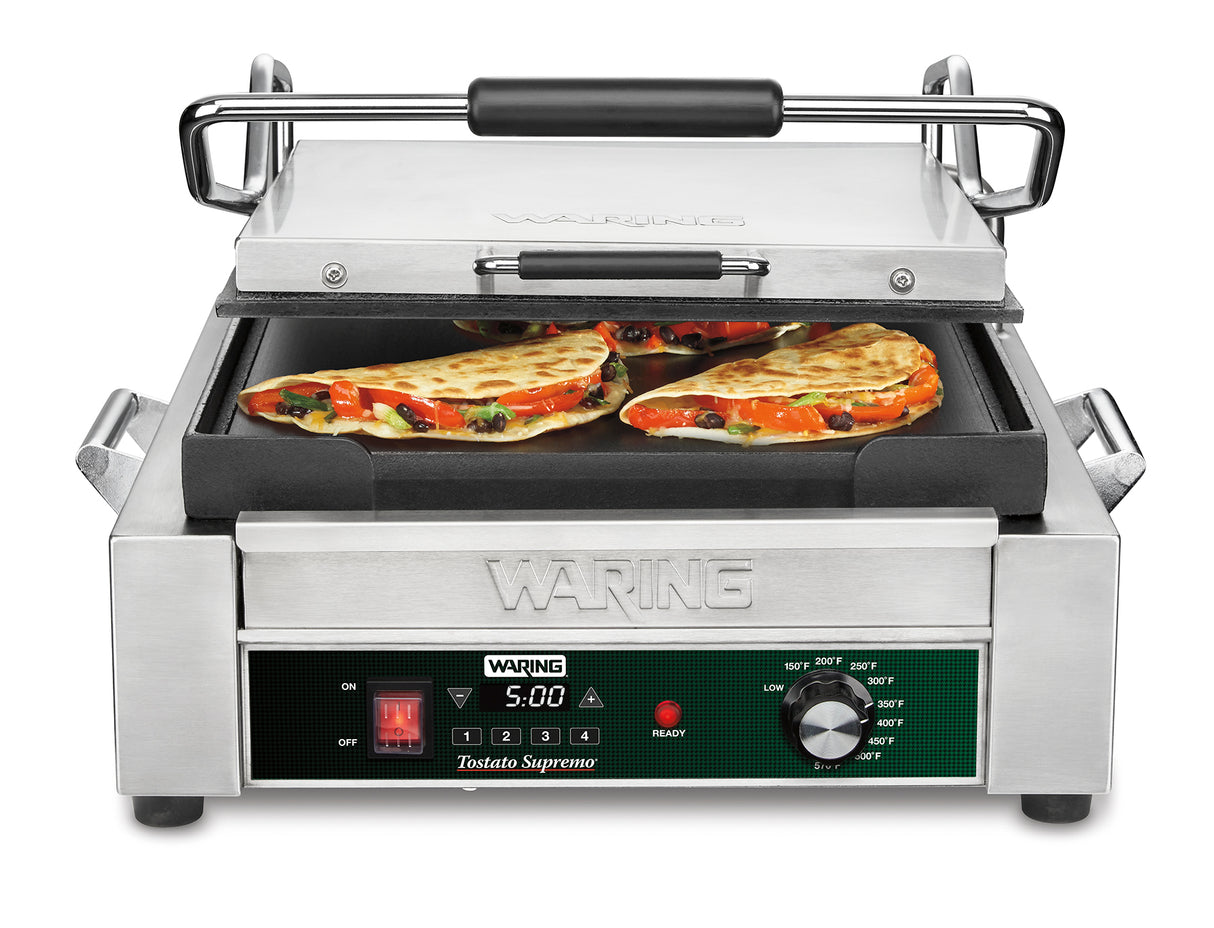 A stainless steel Waring Panini Grill with cast iron plates is open, holding three golden-brown quesadilla slices. The programmable timer displays 5:00, and the press features black handles with labeled buttons and dials. Cheese, peppers, and veggies are visible.
