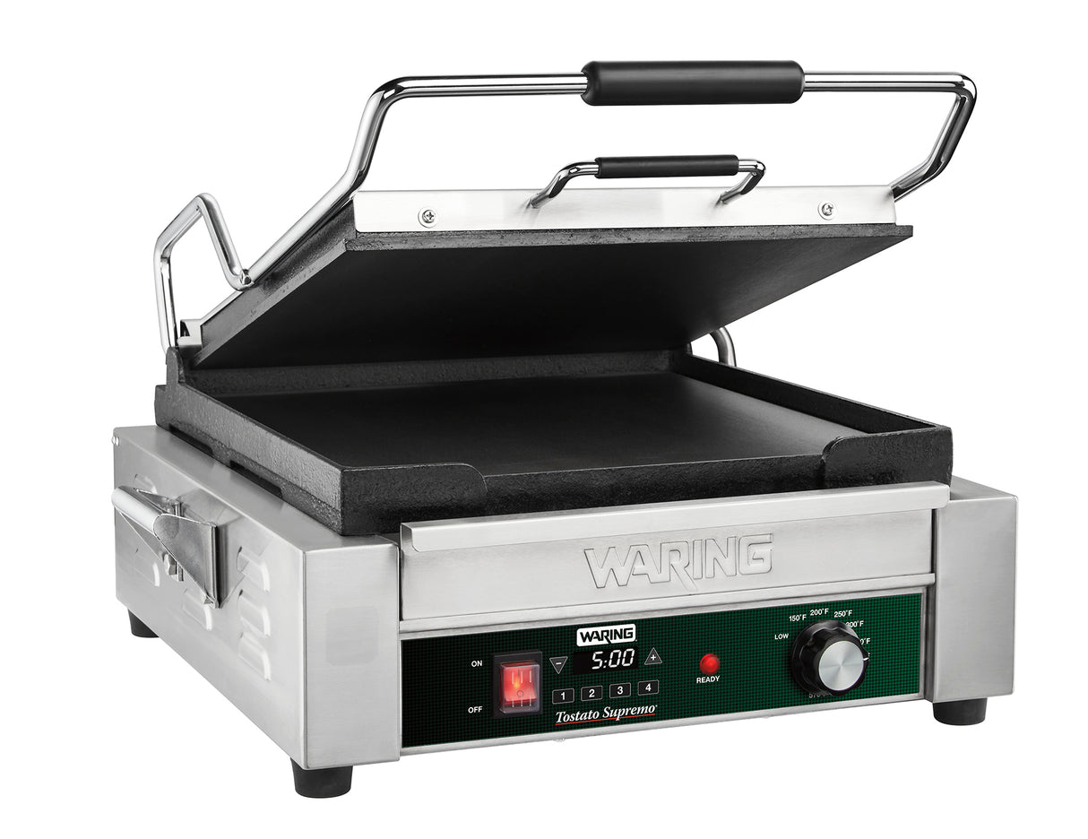 A stainless steel Waring Panini Grill with a black handle and open top grill plate. The front features a programmable timer reading 5:00, a temperature control knob, and on/off switch. The flat lower grill plate is non-stick and ready for use.