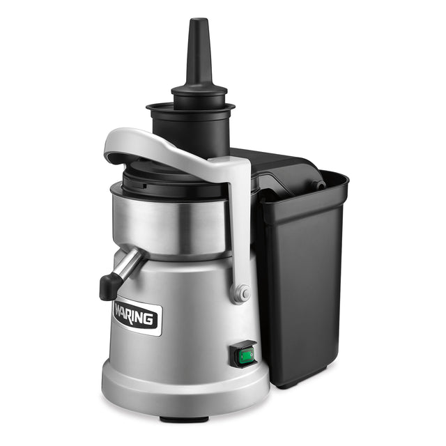 A heavy duty silver and black juice extractor with a cylindrical metal body, continuous pulp ejection, a side handle, top plunger, black plastic pulp container on the side, spout for dispensing juice, and a green power switch at the base.