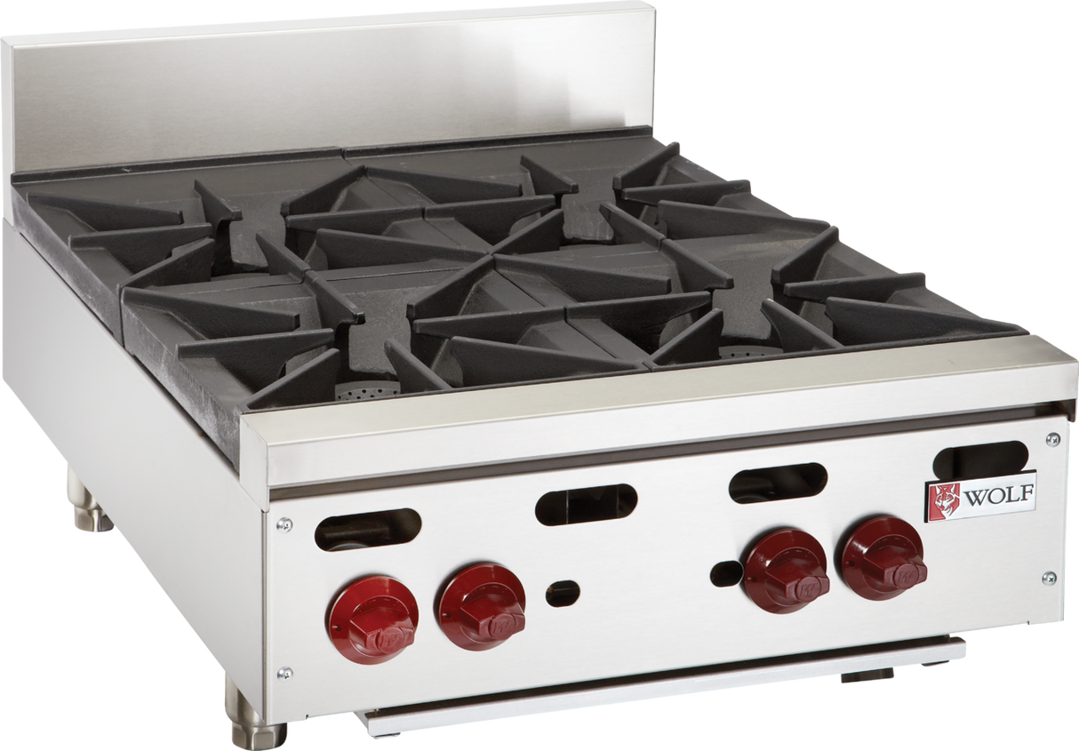 A stainless steel commercial hotplate with four black cast iron burners, red control knobs, and metal legs. The Wolf logo is visible on the front panel. This professional kitchen appliance features a raised backguard and a modern, industrial design.