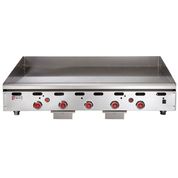 A large commercial stainless steel countertop gas griddle with four red control knobs and a raised backsplash, designed for restaurant use. The front panel features the Wolf brand logo and indicator lights above each knob.