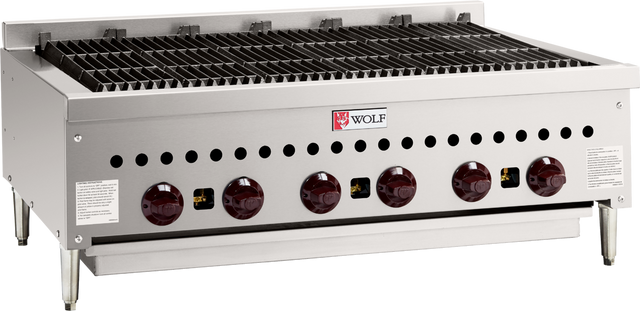 A stainless steel commercial gas charbroiler with six red control knobs, grated grilling surface, Wolf brand logo on the front, and four sturdy legs. Ideal for professional kitchen grilling, with ventilation holes and safety labels on both sides.