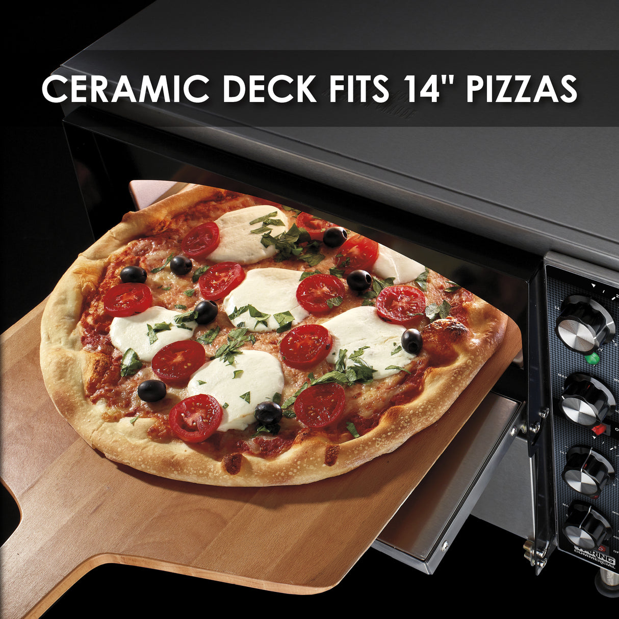 A freshly baked pizza with mozzarella, cherry tomatoes, olives, and basil is being placed into a black electric countertop pizza oven with a wooden peel. Text at the top reads, CERAMIC DECK FITS 14 PIZZAS. Oven controls are visible on the right.