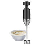 A black and silver Waring Commercial Medium Duty Immersion Blender stands upright next to a white bowl of creamy soup topped with herbs and shredded cheese, against a plain white background. Ideal for blending up to 12 qt capacity.