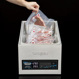 A hand lowers a vacuum-sealed steak into a Waring Sous Vide Circulating Water Bath, which holds other sealed steaks in its spacious 25-liter tank. The display shows 129.0°F and 0:55; programmable memory stations offer precise cooking control.