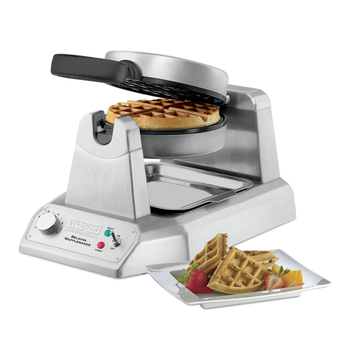 A heavy-duty Belgian Waffle Maker with a circular waffle inside is open, showing its interior. In front, a white plate holds quartered waffles, strawberries, and orange slices. The waffle maker features control knobs and indicator lights on its base.