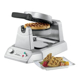 A heavy-duty Belgian Waffle Maker with a circular waffle inside is open, showing its interior. In front, a white plate holds quartered waffles, strawberries, and orange slices. The waffle maker features control knobs and indicator lights on its base.