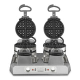 A Commercial Belgian Waffle Maker with independent controls, featuring two non-stick plates open to reveal classic grid patterns. Each side has a handle and rotary knob, plus base indicator lights and branding. The stainless steel unit is clean against a white background.