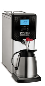 A stainless steel countertop hot water dispenser with a 3 gallon capacity and digital display showing “205°F.” Water pours from a red spout into a matching metal carafe. Features include easy access buttons and a black panel labeled “WARING COMMERCIAL.”.